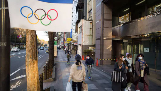 People wearing face masks walk and ride past an Olympics decoration installed along a street in Tokyo.(AP)